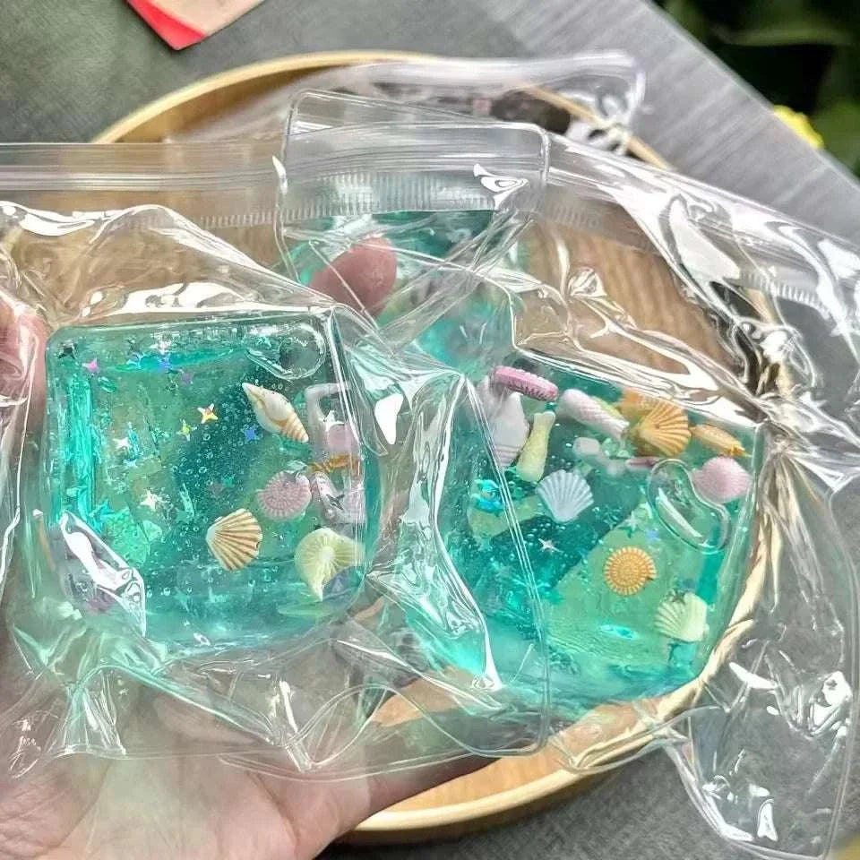 Squishy Ocean Fidget sensory stress ball in translucent turquoise gel with glitter and colorful miniature seashells